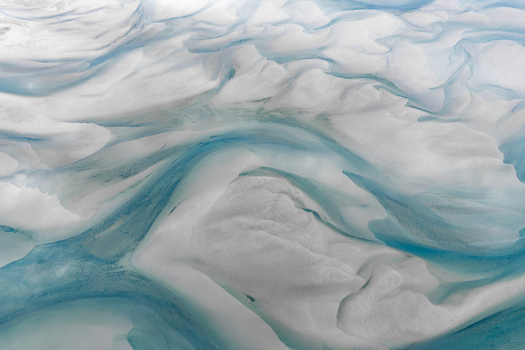 Aerial view of the intricate patterns of white sand and turquoise glacial meltwater channels in the shallow tidal flats of the coastal landscape in Senja Troms Norway.
