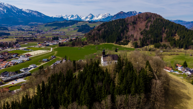 Aerial view of a quaint church nestled atop a hill surrounded by a tapestry of green fields and dense forests with snow capped mountains in the distance Windischgarsten Upper Austria Austria. Aerial view of a quaint church nestled atop a hill surrounded by a tapestry of green fields and dense forests with snow capped mountains in the distance Windischgarsten Upper Austria Austria.