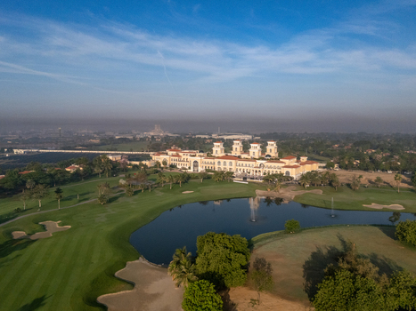 Ahmedabad India 21 March 2026 Aerial view of Kalhaar Blues Greens Golf Club featuring green fairways a central pond with fountains and the clubhouse architecture under a blue sky.