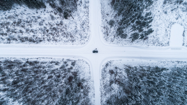 Aerial view of a car stopped at a snowy forest intersection surrounded by pine trees in Latvia. Aerial view of a car stopped at a snowy forest intersection surrounded by pine trees in Latvia.