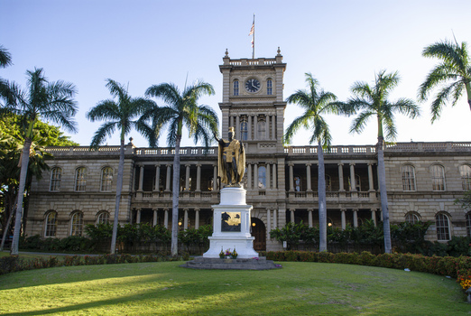 View of the King Kamehameha Statue standing before the historic Aliiolani Hale building surrounded by palm trees and a manicured lawn in Honolulu Hawaii United States.
