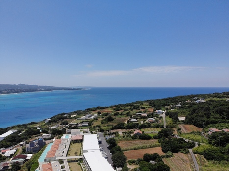 Aerial view of a coastal resort area with white buildings and swimming pools overlooking the turquoise ocean and lush green hills in Nakijin Okinawa Japan. Aerial view of a coastal resort area with white buildings and swimming pools overlooking the turquoise ocean and lush green hills in Nakijin Okinawa Japan.