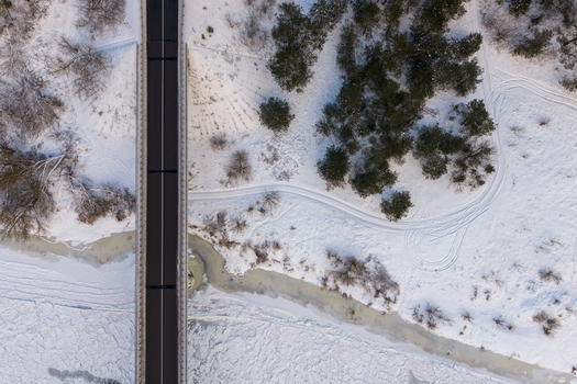 Aerial view of a road bridge crossing a frozen river surrounded by snow covered landscape and pine trees Lithuania. Aerial view of a road bridge crossing a frozen river surrounded by snow covered landscape and pine trees Lithuania.