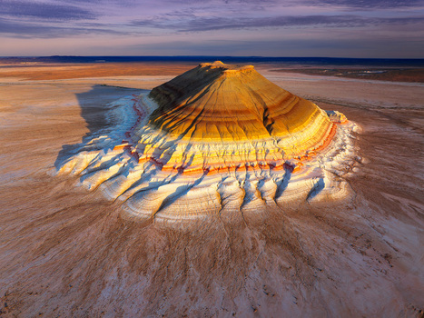 Aerial view of the striking multi colored rock formation casts long shadows over the arid landscape its layered strata painted in hues of yellow orange and white Aktau Kazakhstan.