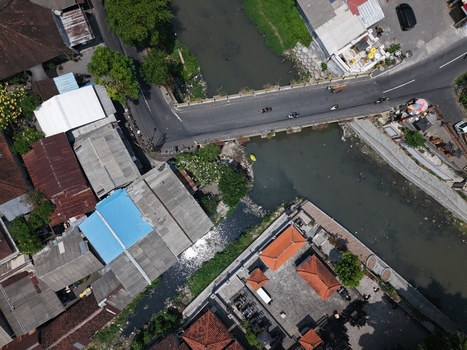Aerial view of a river flowing through a dense urban area with traditional Balinese buildings rooftops and a bridge with traffic in Kecamatan Denpasar Barat Bali Indonesia. Aerial view of a river flowing through a dense urban area with traditional Balinese buildings rooftops and a bridge with traffic in Kecamatan Denpasar Barat Bali Indonesia.
