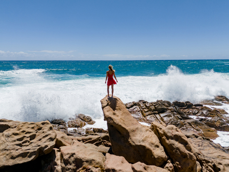 Aerial view of a woman in a red dress standing on a rock at Injidup Natural Spa with crashing waves and turquoise water in Yallingup Western Australia Australia. Aerial view of a woman in a red dress standing on a rock at Injidup Natural Spa with crashing waves and turquoise water in Yallingup Western Australia Australia.