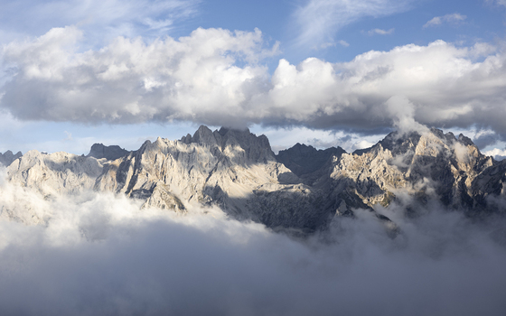 View of jagged peaks pierce through a sea of swirling clouds sunlight catching the stark rock faces creating a dramatic contrast of light and shadow Picos de Europa Asturias Spain. View of jagged peaks pierce through a sea of swirling clouds sunlight catching the stark rock faces creating a dramatic contrast of light and shadow Picos de Europa Asturias Spain.