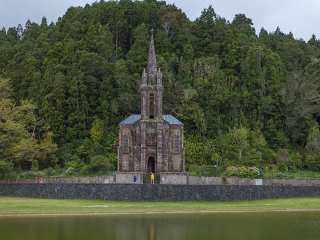 Aerial view of Ermida de Nossa Senhora das Vitorias a historic stone chapel nestled by a lake and surrounded by dense forest with people standing nearby in Furnas Acores Portugal. Aerial view of Ermida de Nossa Senhora das Vitorias a historic stone chapel nestled by a lake and surrounded by dense forest with people standing nearby in Furnas Acores Portugal.