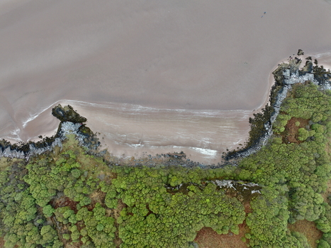 Aerial view of Gruinard Bay featuring the sandy beach dark rocky outcrops and dense green forest under an overcast sky in Gruinard Scotland United Kingdom. Aerial view of Gruinard Bay featuring the sandy beach dark rocky outcrops and dense green forest under an overcast sky in Gruinard Scotland United Kingdom.