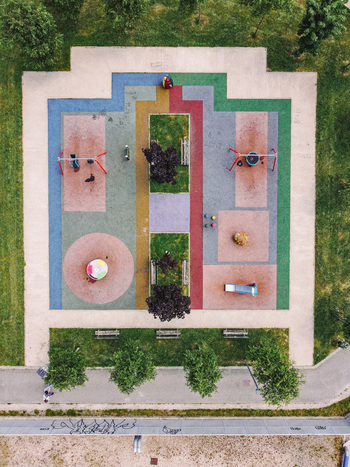 Aerial view of a colorful children s playground with geometric patterns swings and a carousel surrounded by green grass and trees in Turin Piedmont Italy. Aerial view of a colorful children s playground with geometric patterns swings and a carousel surrounded by green grass and trees in Turin Piedmont Italy.