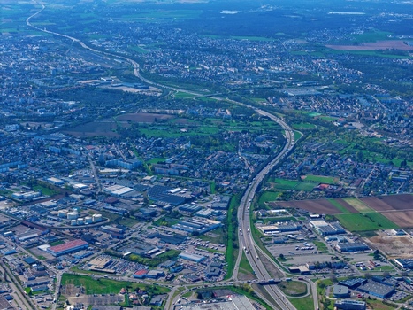 Aerial view of a highway cutting through the landscape a ribbon of grey dividing the green fields and urban sprawl Sausheim Grand Est France.