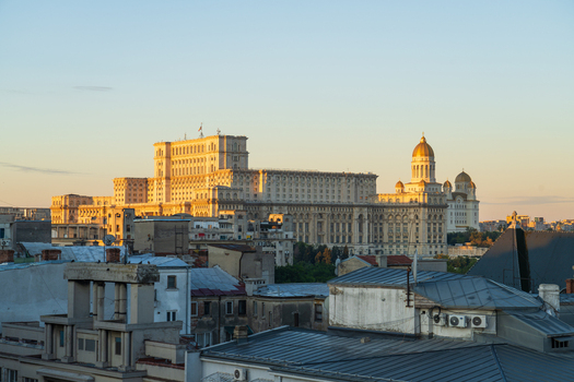 View of the Palace of the Parliament illuminated by golden hour light rising above the urban rooftops of Bucharest Bucharest Romania.