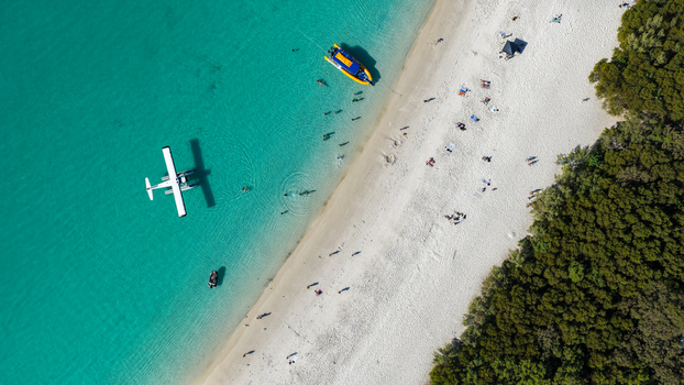Aerial view of Whitehaven Beach with a seaplane floating in turquoise water white sand and people relaxing on the shore in Whitsundays Queensland Australia.