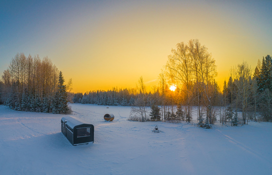Aerial view of a small cabin and a barrel sauna in a snow covered landscape at sunset with birch trees in Latvia. Aerial view of a small cabin and a barrel sauna in a snow covered landscape at sunset with birch trees in Latvia.