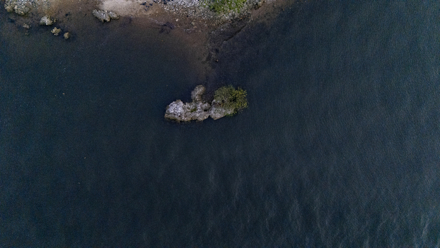 Aerial view of a small rocky islet surrounded by dark rippling water near the shoreline of Badagry Lagos Nigeria. Aerial view of a small rocky islet surrounded by dark rippling water near the shoreline of Badagry Lagos Nigeria.