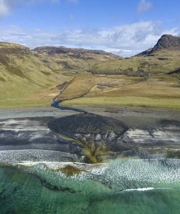 Aerial view of Talisker Bay Beach with a winding river flowing into the turquoise sea surrounded by rugged green hills and dark volcanic sand Isle of Skye Scotland United Kingdom. Aerial view of Talisker Bay Beach with a winding river flowing into the turquoise sea surrounded by rugged green hills and dark volcanic sand Isle of Skye Scotland United Kingdom.