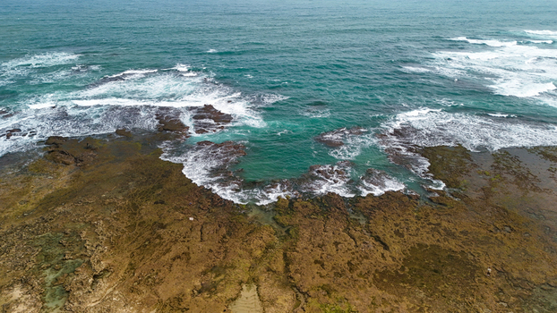 Aerial view of a rocky coastline with turquoise water and waves crashing against the shore in Indonesia.