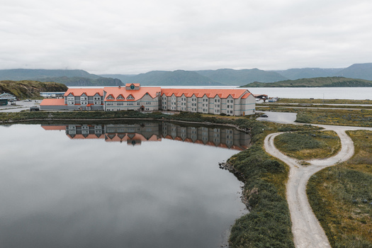 Aerial view of the Grand Aleutian Hotel with its distinctive orange roof reflecting in the calm water surrounded by rolling hills and a dirt road in Unalaska Alaska United States.