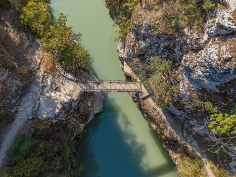 Aerial view of Osumi canyon featuring a pedestrian bridge spanning the turquoise river surrounded by steep rocky cliffs and lush green vegetation Dhores Berat County Albania.