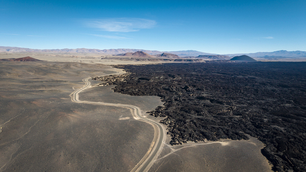 Aerial view of a winding road cutting through a vast volcanic lava field with distant mountains under a clear blue sky in Argentina. Aerial view of a winding road cutting through a vast volcanic lava field with distant mountains under a clear blue sky in Argentina.
