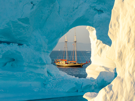 Aerial view of a sailboat framed by a natural arch in a massive iceberg in the Arctic waters of Greenland. Aerial view of a sailboat framed by a natural arch in a massive iceberg in the Arctic waters of Greenland.