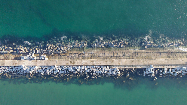 Aerial view of the stone breakwater with large boulders protecting the concrete jetty from the turquoise Atlantic Ocean waters in Ferragudo Faro District Portugal.