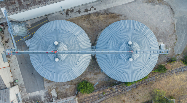 Aerial view of two large circular grain silos connected by an overhead conveyor system showcasing modern agricultural storage infrastructure in Le Pouzin Auvergne Rhone Alpes France.
