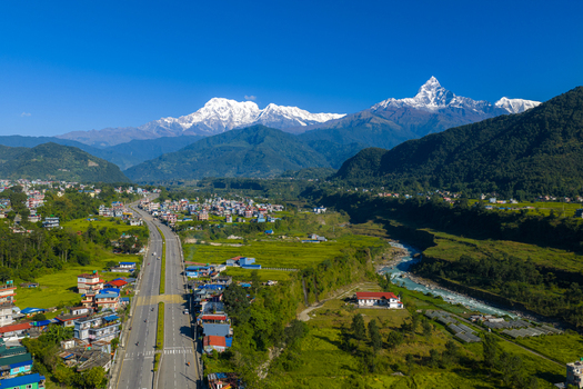 Aerial view of the majestic Machapuchare mountain peak towering over a winding river a modern road and lush green settlements Nepal.