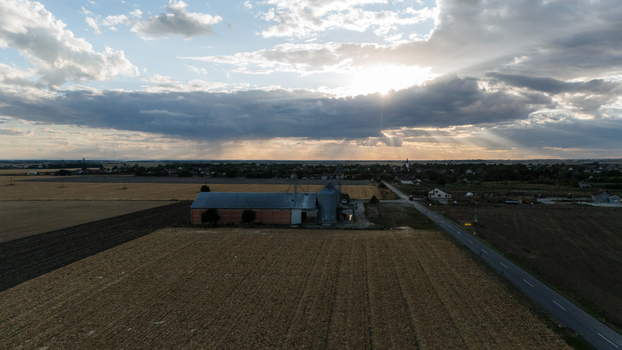 Aerial view of a rural agricultural facility with silos and barns surrounded by harvested fields and a road under a dramatic sunset sky in Veliki Radinci Vojvodina Serbia. Aerial view of a rural agricultural facility with silos and barns surrounded by harvested fields and a road under a dramatic sunset sky in Veliki Radinci Vojvodina Serbia.