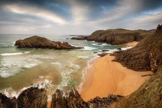 View of Boyeeghter Bay with its golden sand beach and the rugged rocky cliffs under a cloudy sky Ireland.
