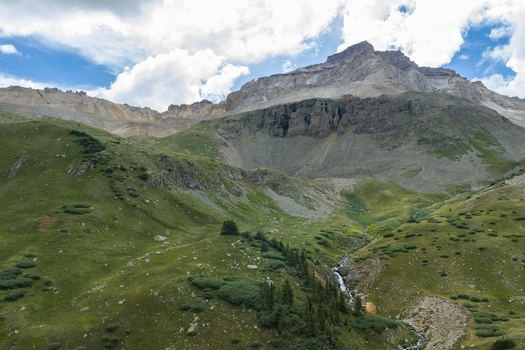 Aerial view of Mount Sneffels in the San Juan Mountains featuring green slopes rocky peaks and a stream in Yankee Boy Basin in Ouray County Colorado United States. Aerial view of Mount Sneffels in the San Juan Mountains featuring green slopes rocky peaks and a stream in Yankee Boy Basin in Ouray County Colorado United States.