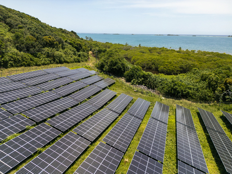 Aerial view of a large solar panel farm situated on a lush green hillside overlooking the turquoise Caribbean Sea in Guanaja Bay Islands Department Honduras.