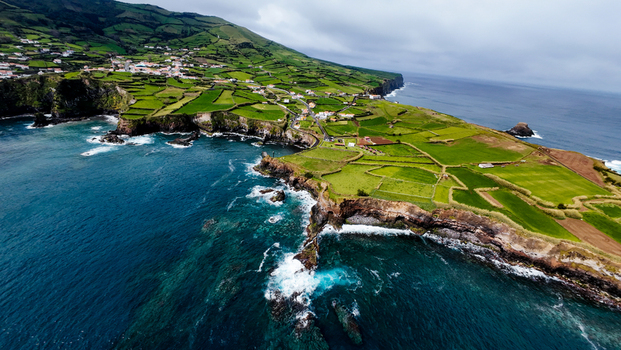 Aerial view of the rugged coastline meeting the vast ocean with the green farmlands stretching inland Flores A&ccedil;ores Portugal.
