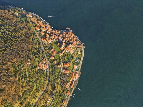 Aerial view of Monte Isola featuring red tiled rooftops lush green forests and a boat on the calm blue water of Lake Iseo Monte Isola Lombardy Italy. Aerial view of Monte Isola featuring red tiled rooftops lush green forests and a boat on the calm blue water of Lake Iseo Monte Isola Lombardy Italy.