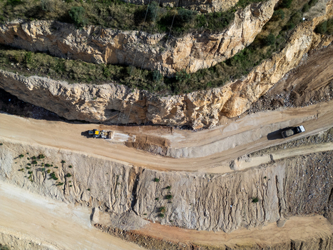 Aerial view of a bulldozer working on a dirt road carved into a rocky hillside at a quarry in Teulada Valencian Community Spain.