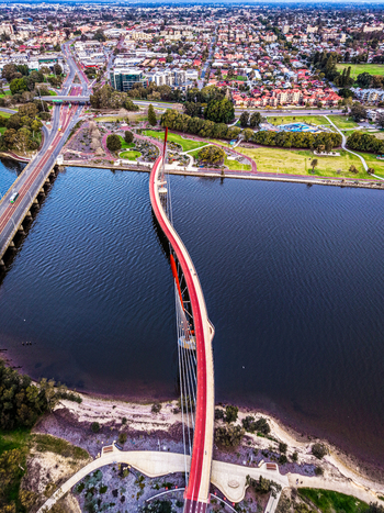 Aerial view of Boorloo Bridge spanning the Swan River with its distinctive red pedestrian path and cable stayed design surrounded by urban parklands in East Perth Western Australia Australia.