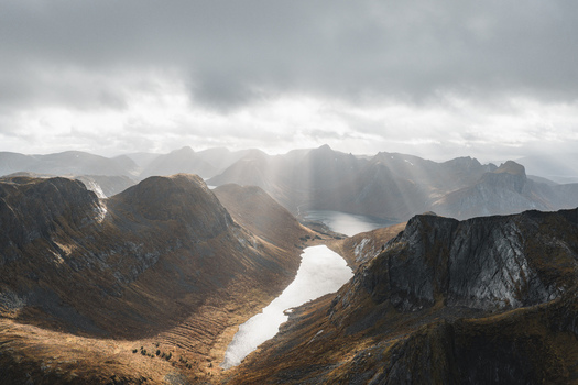 Aerial view of the dramatic mountain landscape with glacial lakes rugged peaks and sunbeams breaking through clouds in Senja Troms Norway.