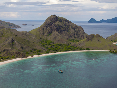 Aerial view of Komodo National Park with rugged hills white sand beach and turquoise waters with a boat in Komodo East Nusa Tenggara Indonesia. Aerial view of Komodo National Park with rugged hills white sand beach and turquoise waters with a boat in Komodo East Nusa Tenggara Indonesia.