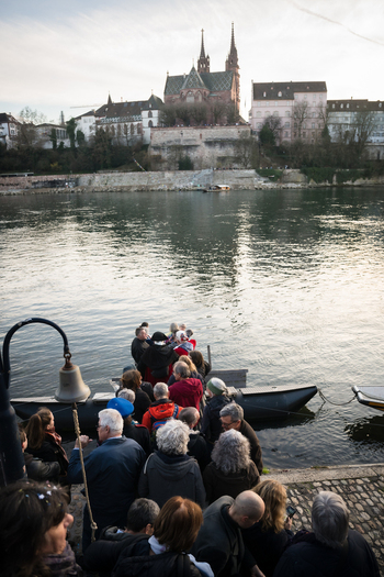Basel Switzerland 10 March 2025 View of the bustling riverbank as people gather near a small boat with the Basel Munster cathedral standing tall in the background. Basel Switzerland 10 March 2025 View of the bustling riverbank as people gather near a small boat with the Basel Munster cathedral standing tall in the background.