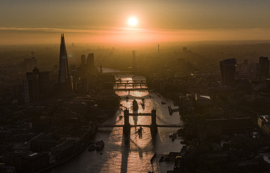Aerial view of Tower Bridge and The Shard along the River Thames during a golden sunset with hazy urban skyline in London Greater London United Kingdom. Aerial view of Tower Bridge and The Shard along the River Thames during a golden sunset with hazy urban skyline in London Greater London United Kingdom.