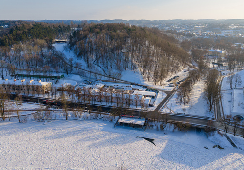 Aerial view of a snow covered landscape featuring a frozen river a road bridge and a wooded hill under bright winter sunlight in Vilnius County Lithuania.