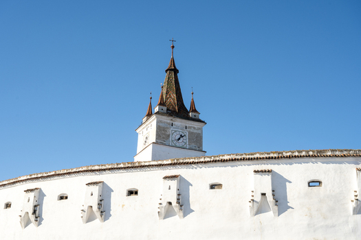 View of the historic Prejmer Fortified Church with its white defensive walls and clock tower under a clear blue sky in Prejmer Brasov Romania. View of the historic Prejmer Fortified Church with its white defensive walls and clock tower under a clear blue sky in Prejmer Brasov Romania.