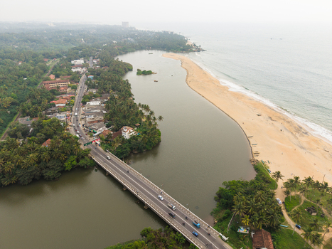 Aerial view of a bridge crossing a river estuary near the sandy coastline and lush tropical greenery in Galle Southern Province Sri Lanka.