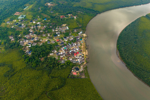 Aerial view of Opobo Town nestled along a winding river surrounded by dense mangrove forests featuring residential buildings and small pathways Opobo Town Rivers Nigeria. Aerial view of Opobo Town nestled along a winding river surrounded by dense mangrove forests featuring residential buildings and small pathways Opobo Town Rivers Nigeria.