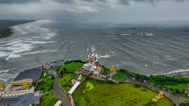 Aerial view of the giant Shiva statue at Murudeshwar Temple overlooking the Arabian Sea with lush green grounds and stormy skies in Murdeshwar Karnataka India.