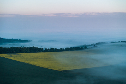 Aerial view of Nuffield countryside in the Chiltern Hills with yellow rapeseed fields and rolling hills partially covered by thick morning fog Nuffield Oxfordshire United Kingdom. Aerial view of Nuffield countryside in the Chiltern Hills with yellow rapeseed fields and rolling hills partially covered by thick morning fog Nuffield Oxfordshire United Kingdom.