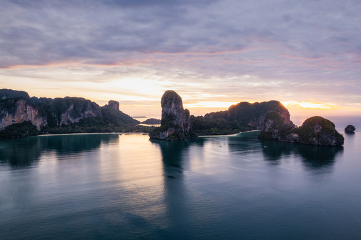 Aerial view of Railay Beach with dramatic limestone cliffs rising from the calm sea under a soft sunset sky in Ao Nang Krabi Thailand. Aerial view of Railay Beach with dramatic limestone cliffs rising from the calm sea under a soft sunset sky in Ao Nang Krabi Thailand.
