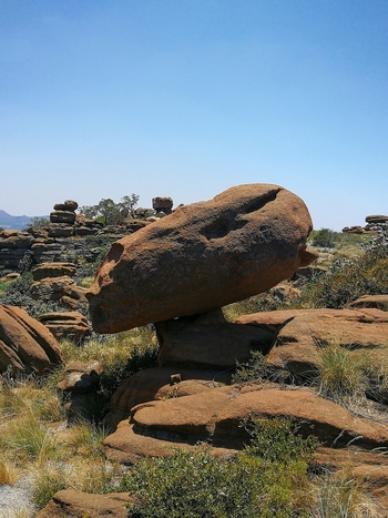 View of a unique rock formation balanced on a rocky outcrop in the Mountain Sanctuary surrounded by dry grass and shrubs under a clear blue sky in Mooinooi North West South Africa.