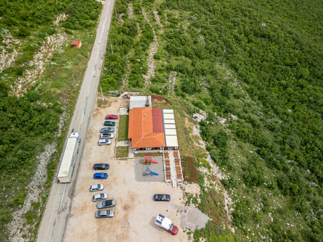 Vlahinja Bosnia and Herzegovina 29 May 2025 Aerial view of Restoran Vlahinja with a parking lot cars a nearby road with a truck and a small playground set amidst green hills.