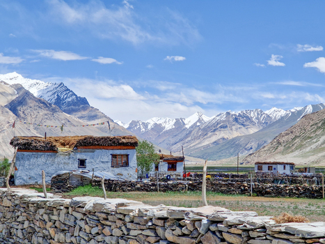 View of traditional stone houses with mud brick walls and thatched roofs set against a backdrop of snow capped mountains near the Penzi La road in Zanskar Ladakh India.